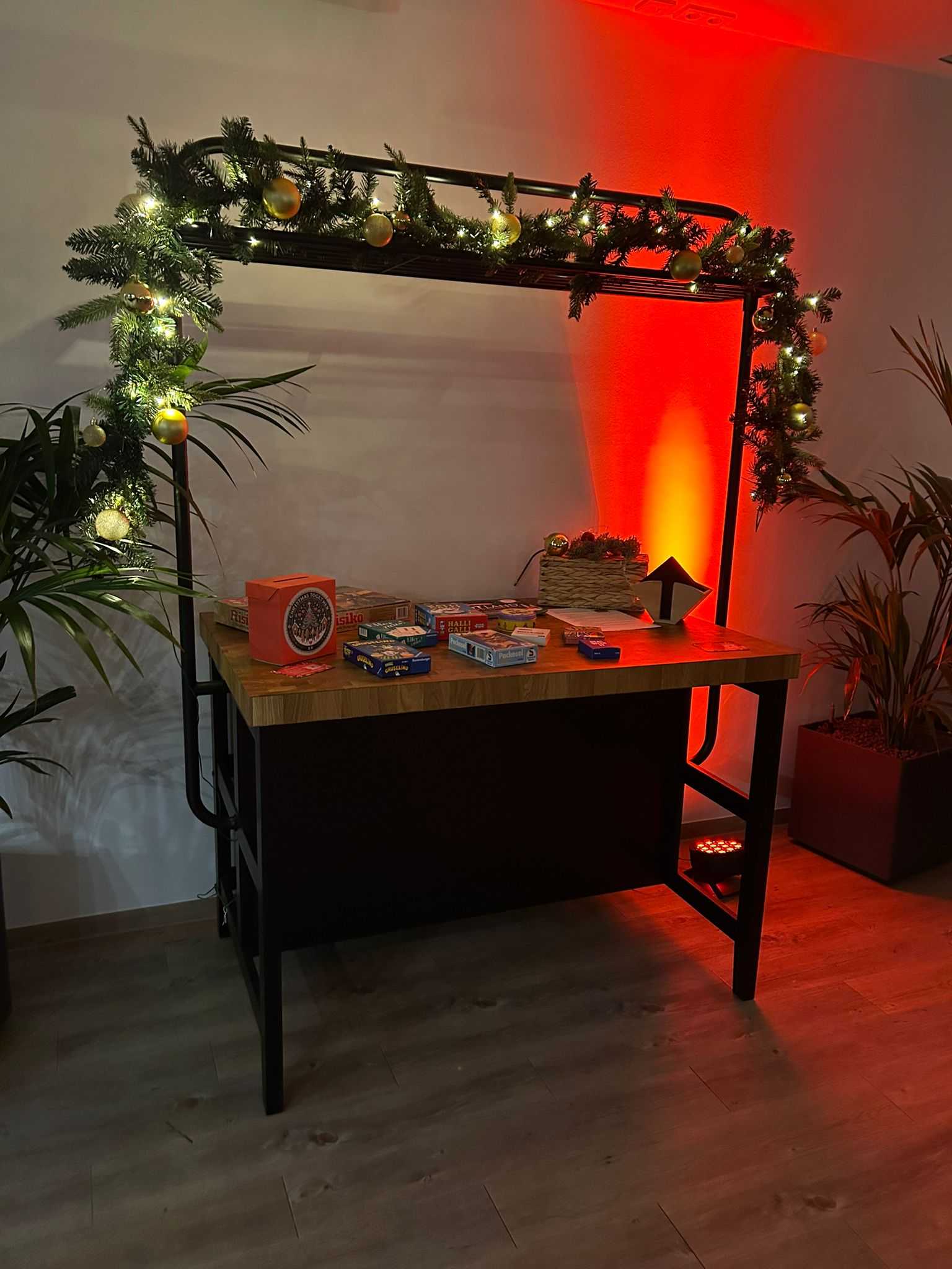 Mit Tannengirlande und Lichterkette geschmückter Tisch mit Brettspielen und Spendenbox in rotem Lichtschein