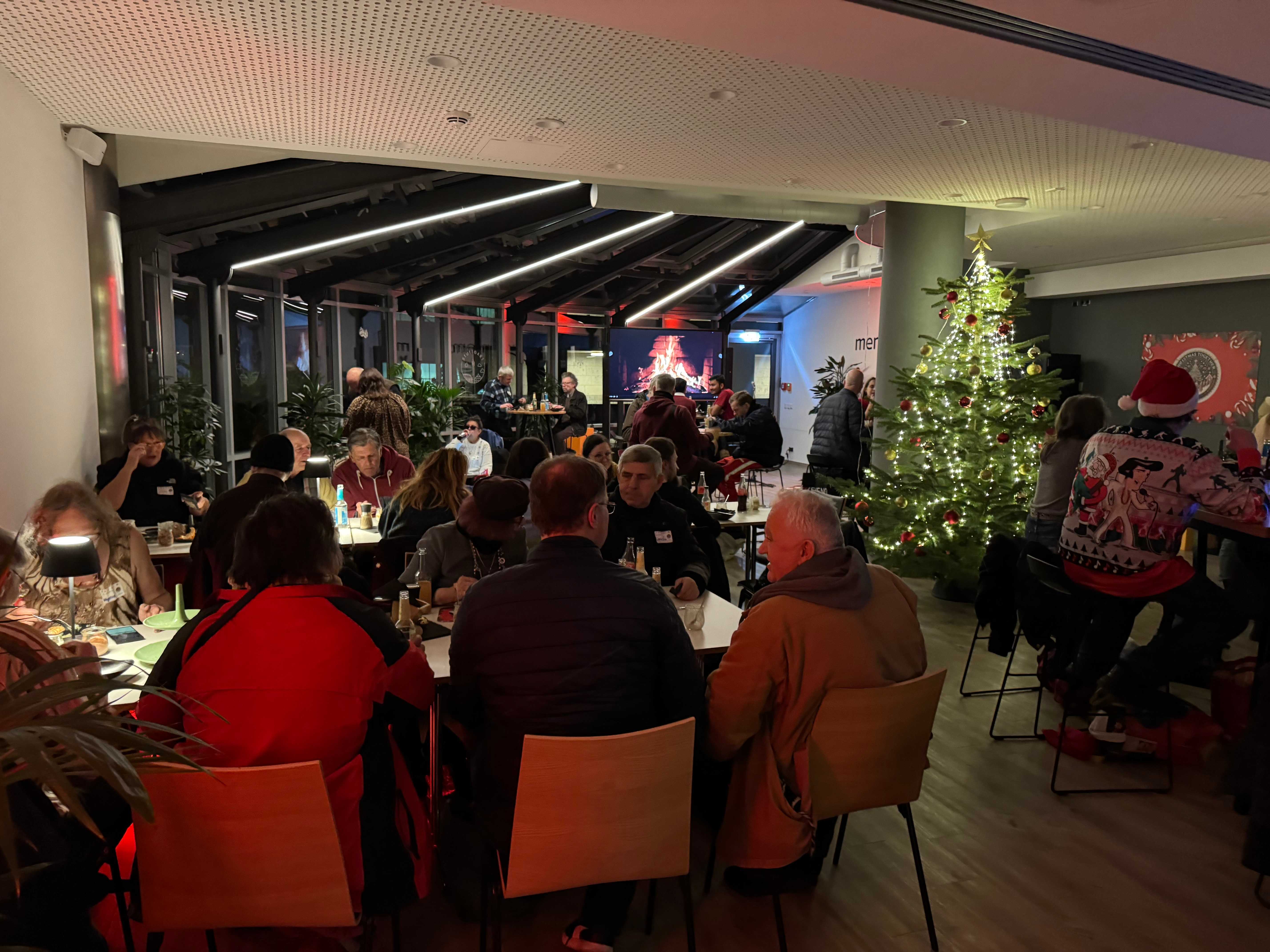 Voller Saal: Gäste feiern gemeinsam an langen Tischen neben dem leuchtenden Weihnachtsbaum