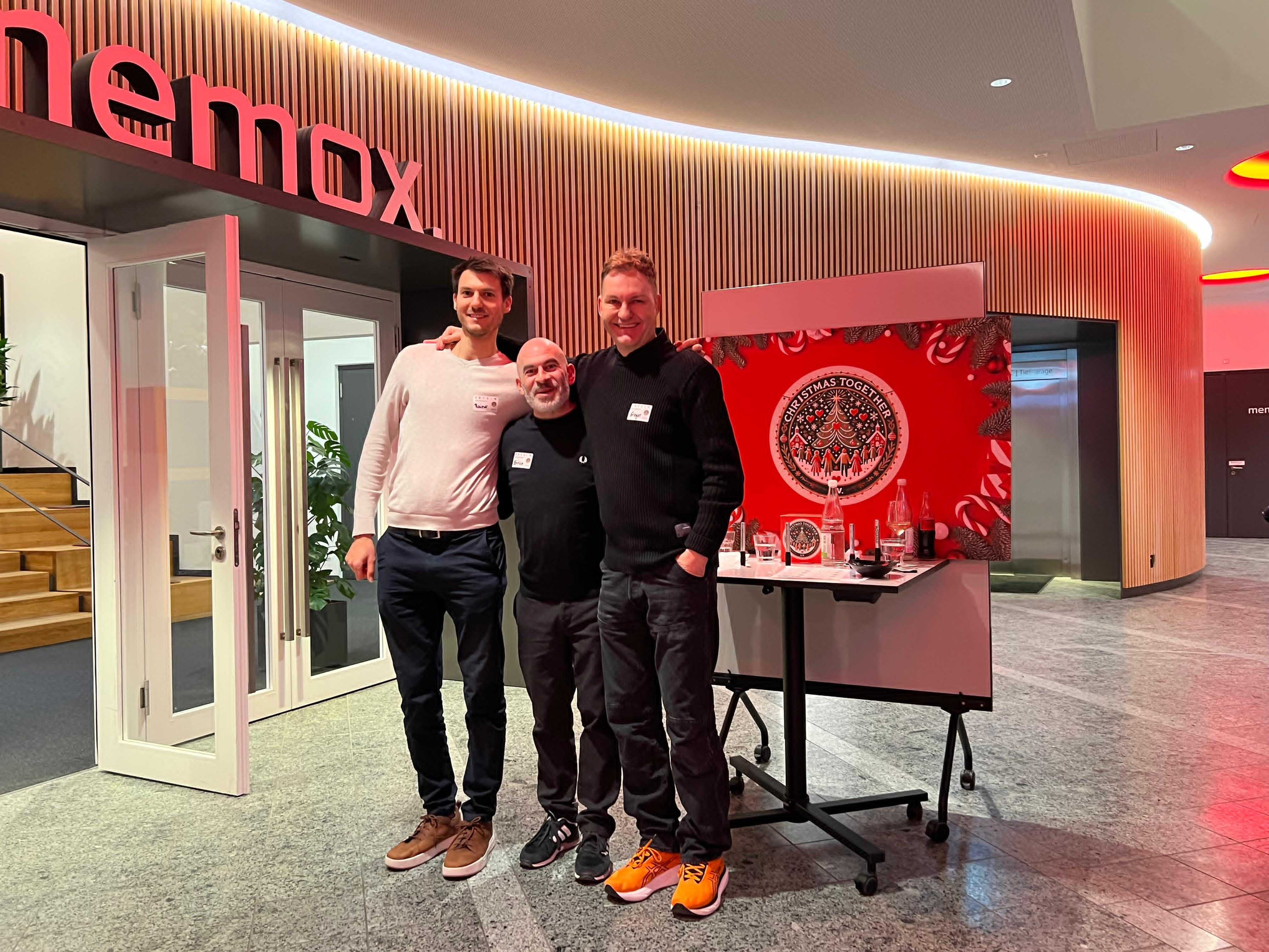 Drei Helfer vor dem Eingang bei memox neben der roten Christmas-Together-Tafel